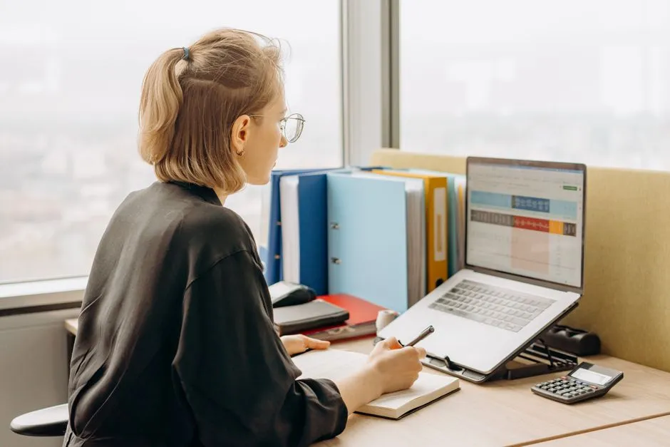 A person working through a spreadsheet on a laptop at a desk, illustrative stock photo.